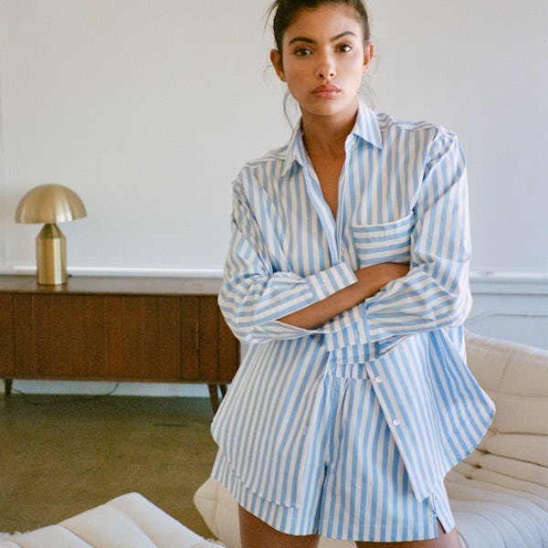 a model wearing an oversize striped button-down shirt with jeans and flats on the beach