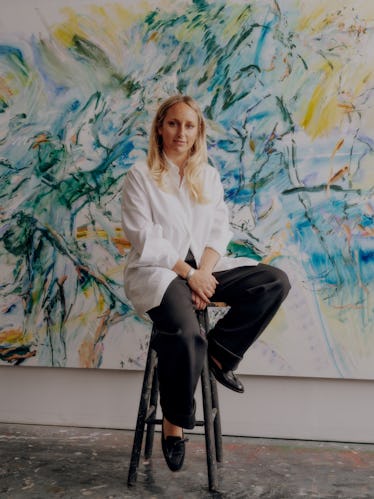 Kylie sitting on a stool in front of her painting "The Places We Once Called Home"