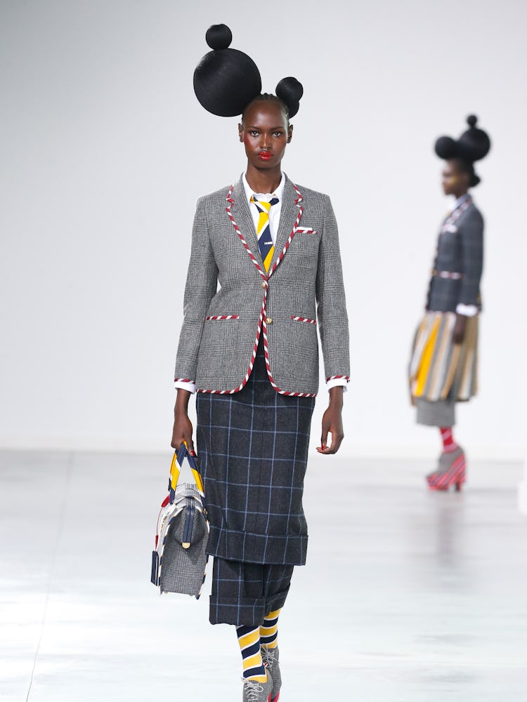 A model walking the runway in a grey blazer and dark blue checkered skirt 