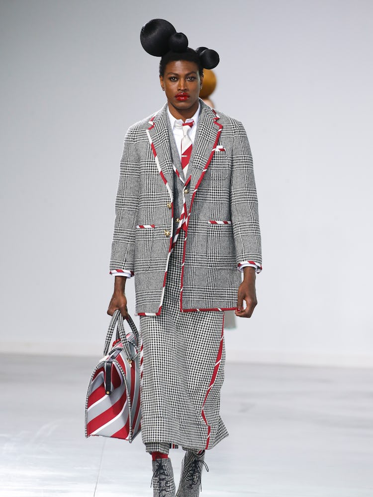 A model walking the Thom Browne Fall 202 runway in a grey blazer and skirt with a matching bag 