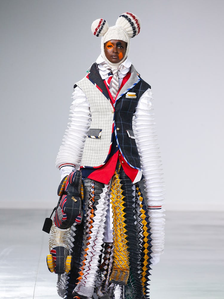 A model walking the Thom Browne Fall 2022 runway in a layered multicolored coat and skirt 