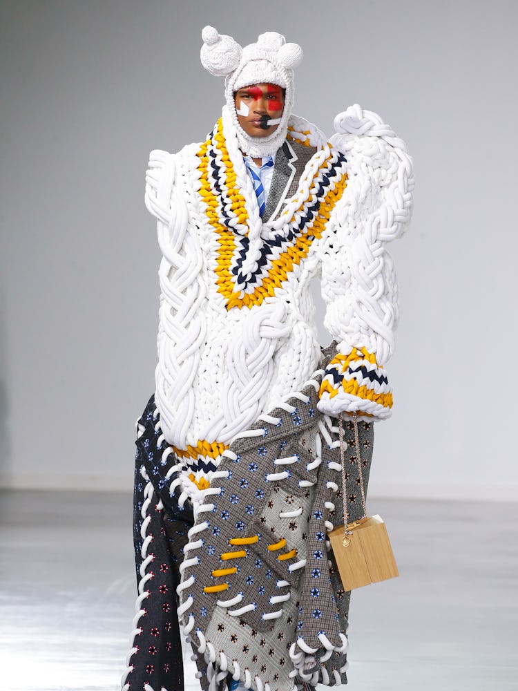 A model walking in an oversized white knit vest, grey skirt and headpiece with ears for Thom Browne ...
