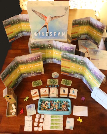 A birds-eye view (pun intended) of the Wingspan board game laid out on a wooden table, showing its d...