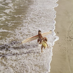 Young couple with surf board running on beach