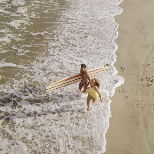 Young couple with surf board running on beach