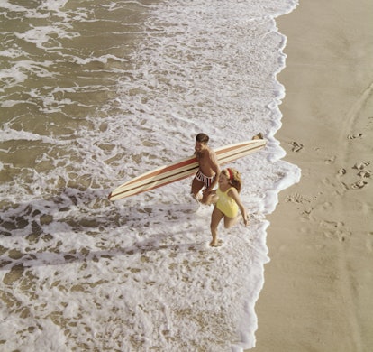 Young couple with surf board running on beach