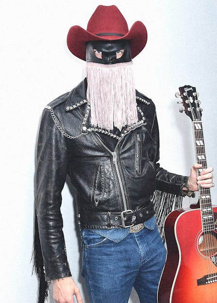 Orville Peck in a black leather jacket, red cowboy hat, facemask with glitter fringe and blue denim ...