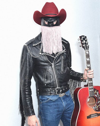 Orville Peck in a black leather jacket, red cowboy hat, facemask with glitter fringe and blue denim ...