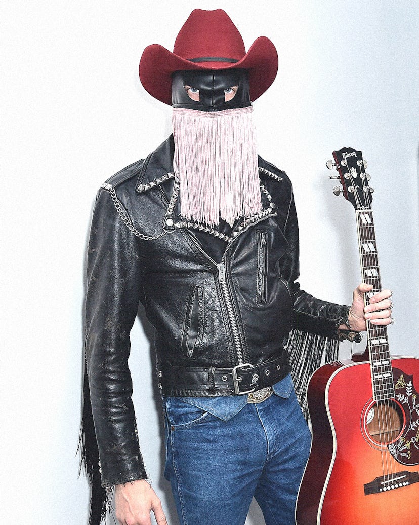 Orville Peck in a black leather jacket, red cowboy hat, facemask with glitter fringe and blue denim ...