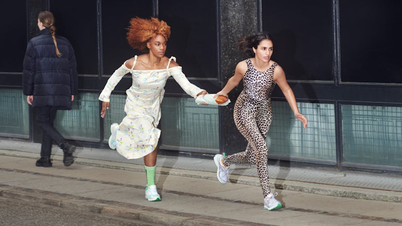 Two models run the street, holding hands, both wearing the Ganni and New Balance's Y2K Sneaker.