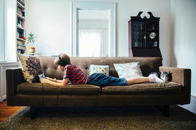 A young boy with headphones using his phone while lying on a brown couch