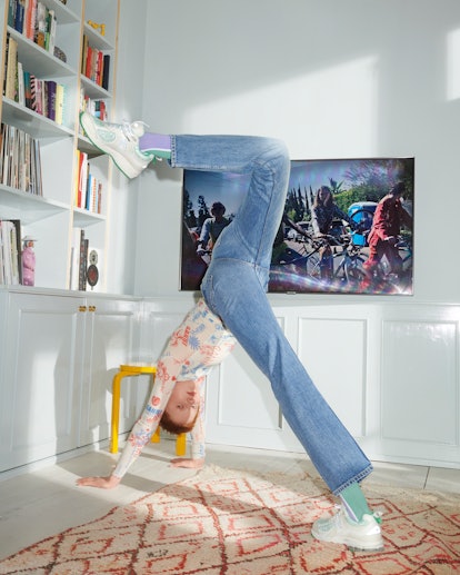 The model does in-house yoga dressed in jeans, a shirt, and Ganni And New Balance's Y2K Sneakers. 