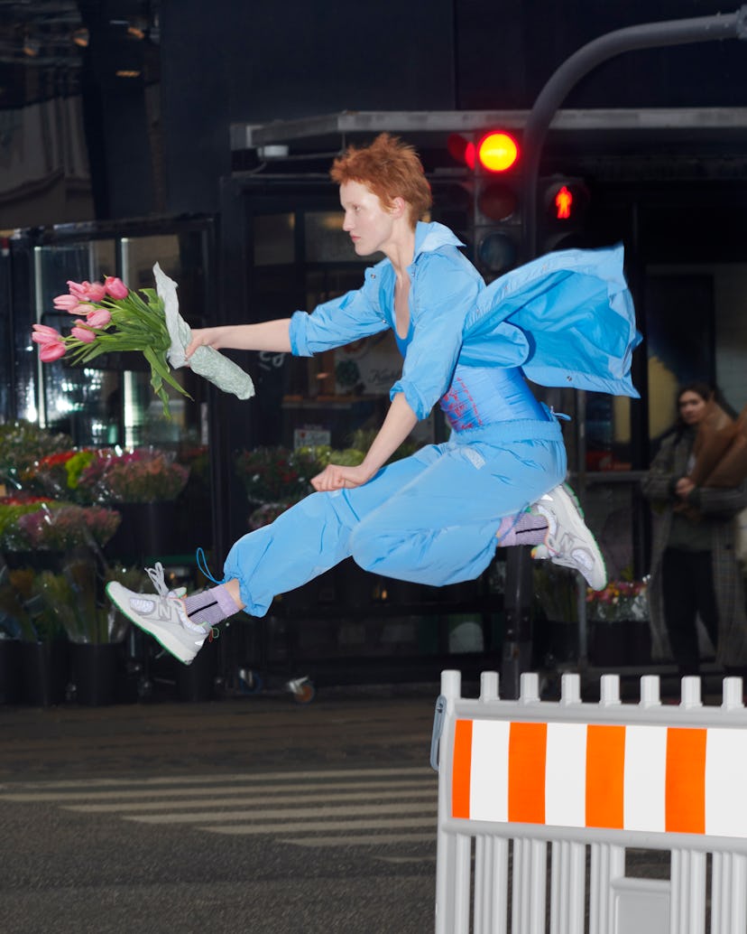 The model jumps over the fence while she holds the flowers in Ganni and New Balance's new sneakers.