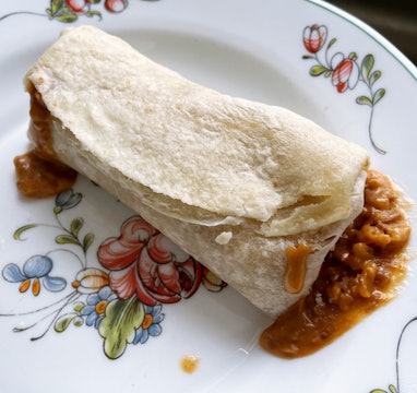 Frozen burrito leaking filling on a plate.