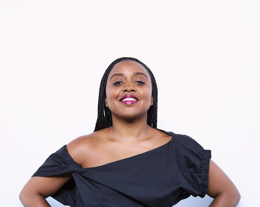 Quinta Brunson stands akimbo, smiling with her chin up in an off-the-shoulder-black dress.