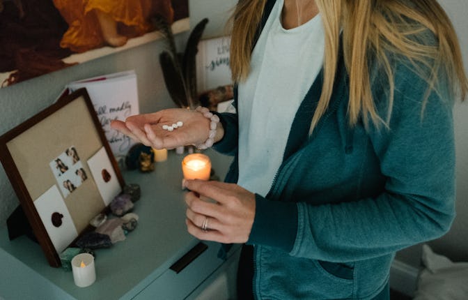 A girl holding four abortion pills, standing next to a dresser with a lit up candle on it.
