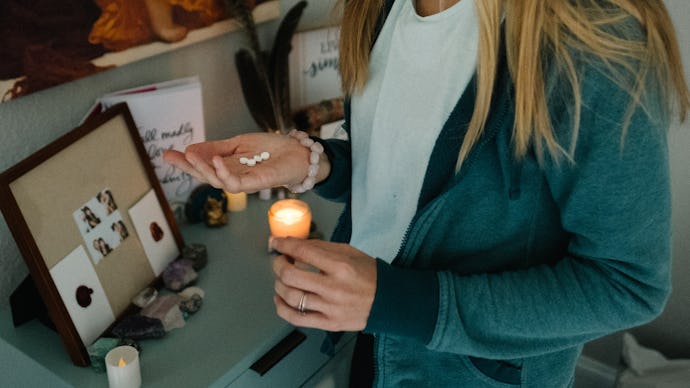 A girl holding four abortion pills, standing next to a dresser with a lit up candle on it. 