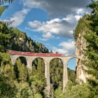 Stunning train trip where the train goes over a bridge overlooking a beautiful natural view.