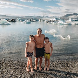 Chris Burkard and his two sons at a rocky beach, with glaciers in the background.
