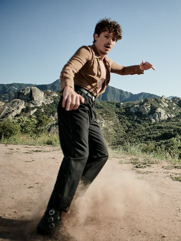 The actor sliding through sand and brings the dust up in a shirt, pants and shoes by Saint Laurent a...