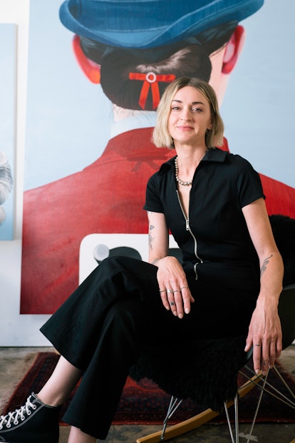 Sarah Miska sitting in a rocking chair in front of one of her paintings 