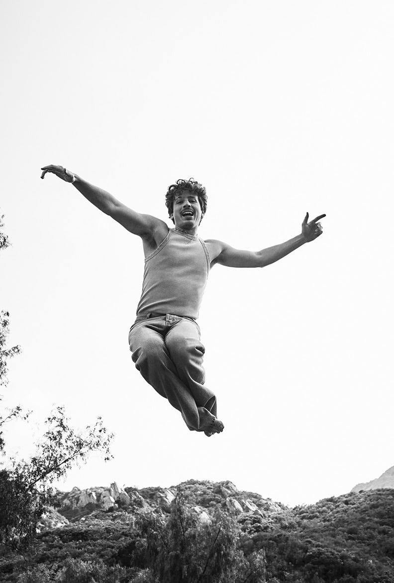 Black and white photo of Charlie Puth in a EYTYS tank and jeans jumping around in a field