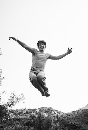 Black and white photo of Charlie Puth in a EYTYS tank and jeans jumping around in a field 