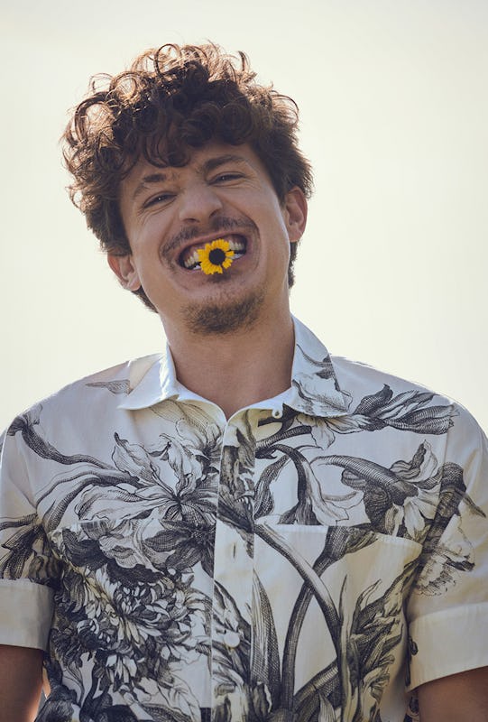 Charlie smiling with a small sunflower in his teeth wearing a white flower shirt by Erdem