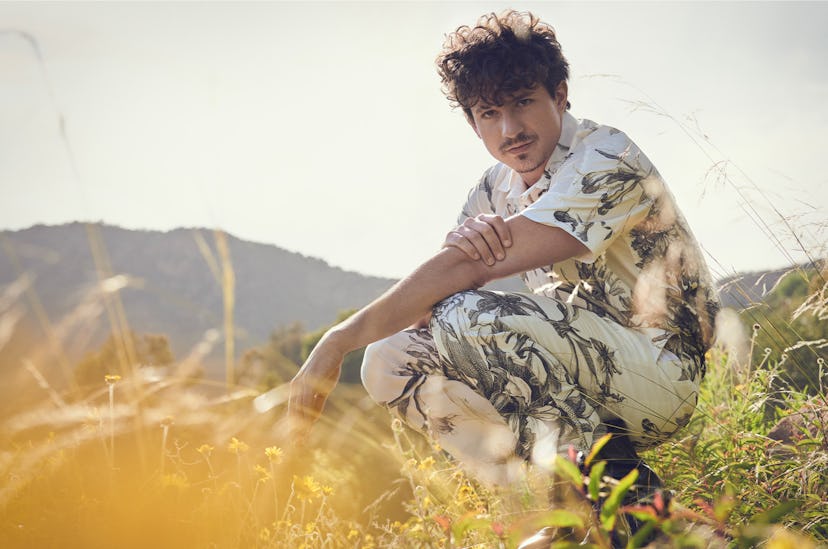 Charlie Puth in a white flower motive set of a button-up and pants posing in a field