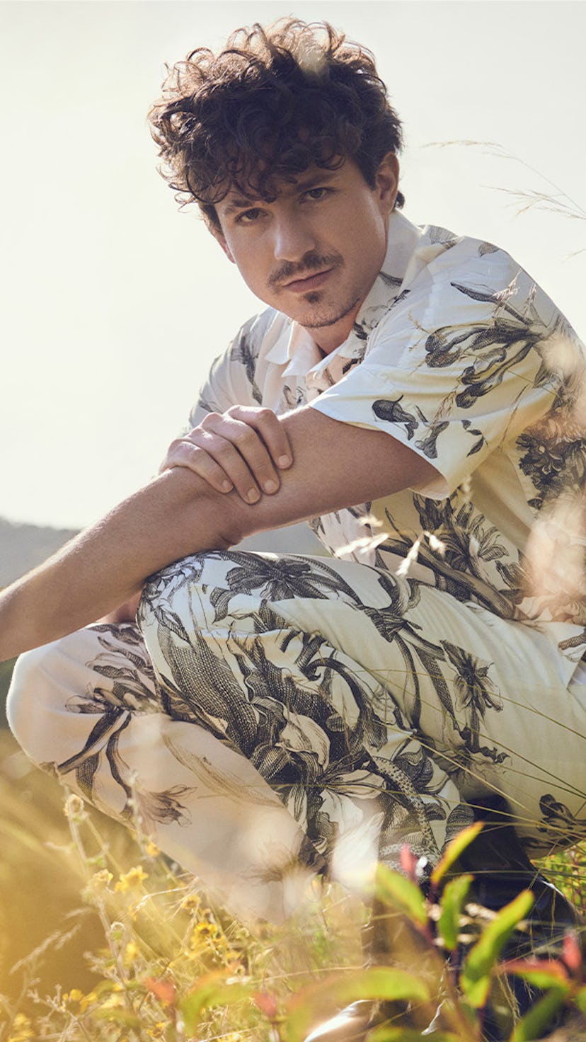 Charlie Puth in a white flower motive set of a button-up and pants posing in a field
