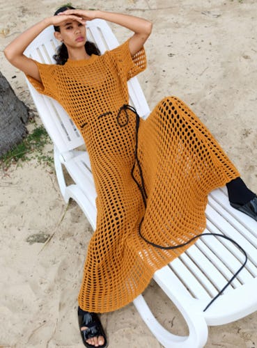 A model in an orange maxi mesh dress lying on a beach decker chair