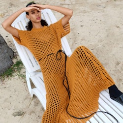 A model in an orange maxi mesh dress lying on a beach decker chair