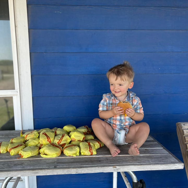 A 2-year-old grinning and holding a McDonald's cheeseburger after ordering 31 of them through DoorDa...