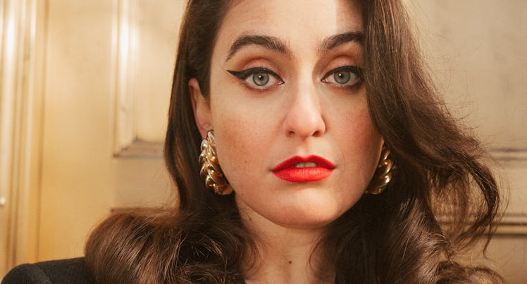 Comedian Catherine Cohen wearing a blazer, red lipstick and gold earrings.