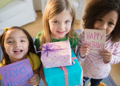 Three smiling young girls looking up to face camera and holding an upside down handmade birthday car...