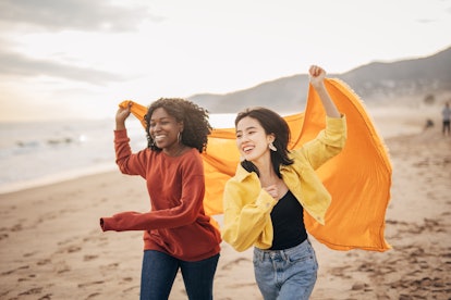 Two young women running on the beach after reading their May 23, 2022 weekly horoscope