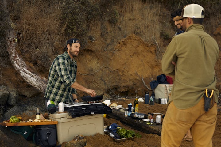 Three men talking and standing around an outdoor grill