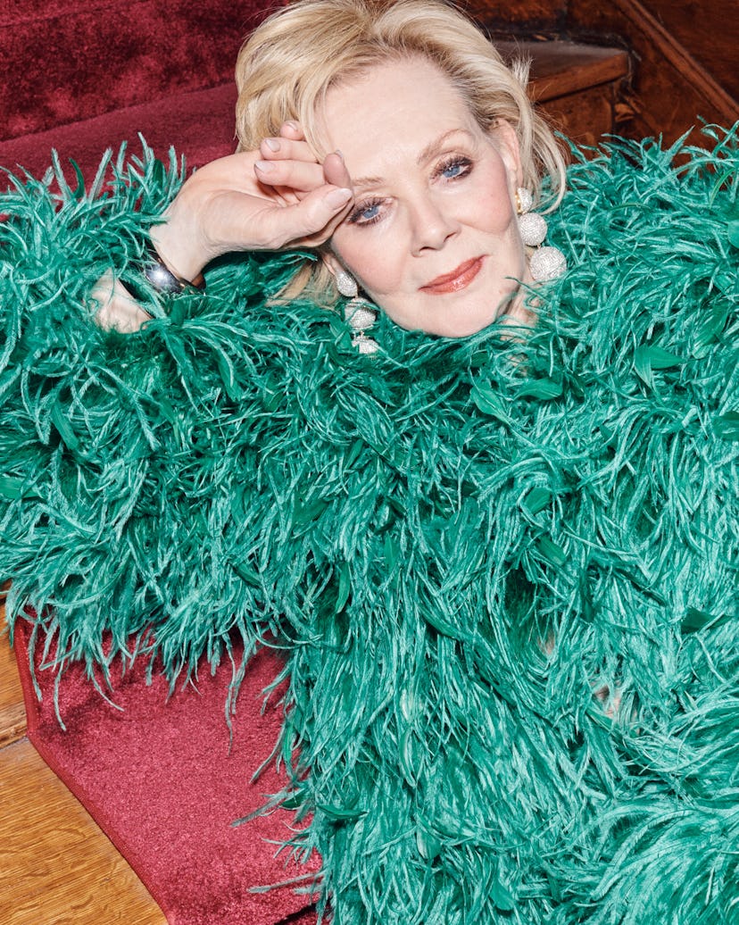 Jean Smart in a green feathered Valentino coat and Rebecca De Ravenel earrings, lounging on the red ...