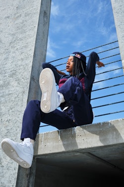 A street dancer sitting on a concrete wall holding on to bars behind her