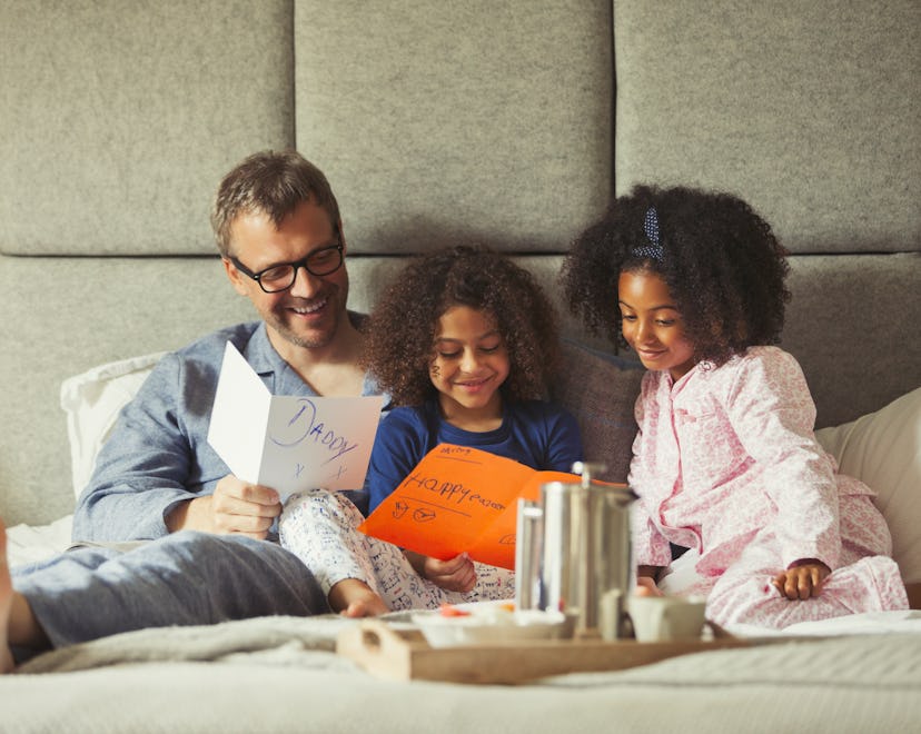 dad having breakfast in bed with daughters, laughing at funny thing to write in father's day card