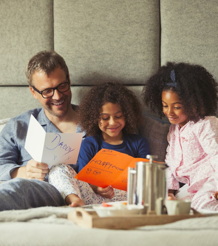 dad having breakfast in bed with daughters, laughing at funny thing to write in father's day card 