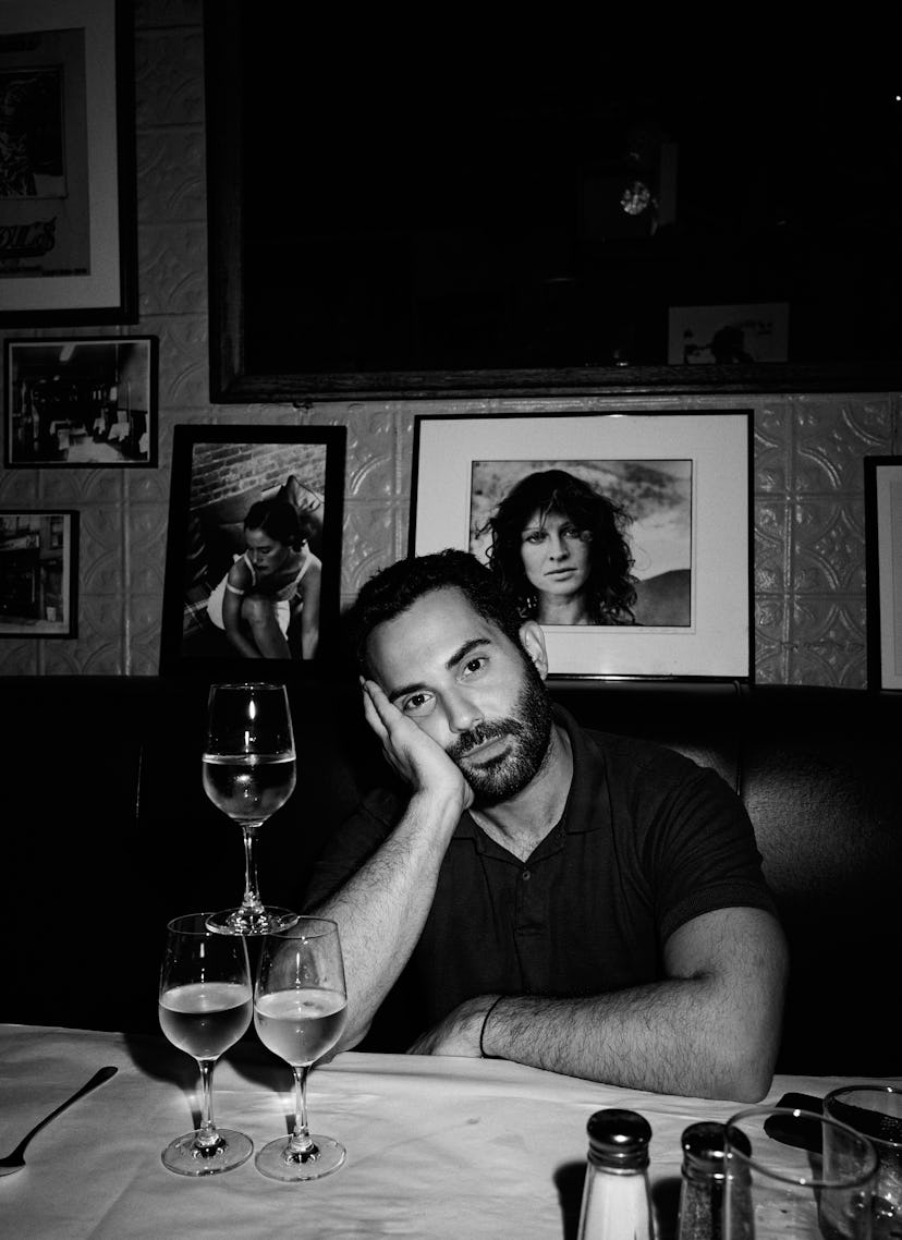 The chef and writer Andy Baraghani sitting at a restaurant table with his hand to his cheek