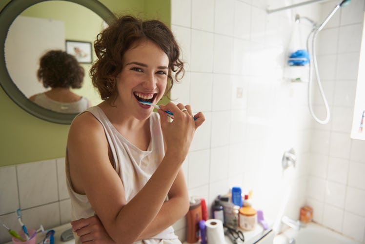 Young woman brushing her teeth in her new bathroom after splurging on items for her first apartment.