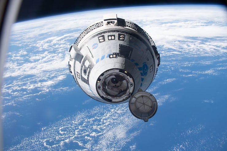 Starliner capsule docks at the ISS in space with the earth visible in the background