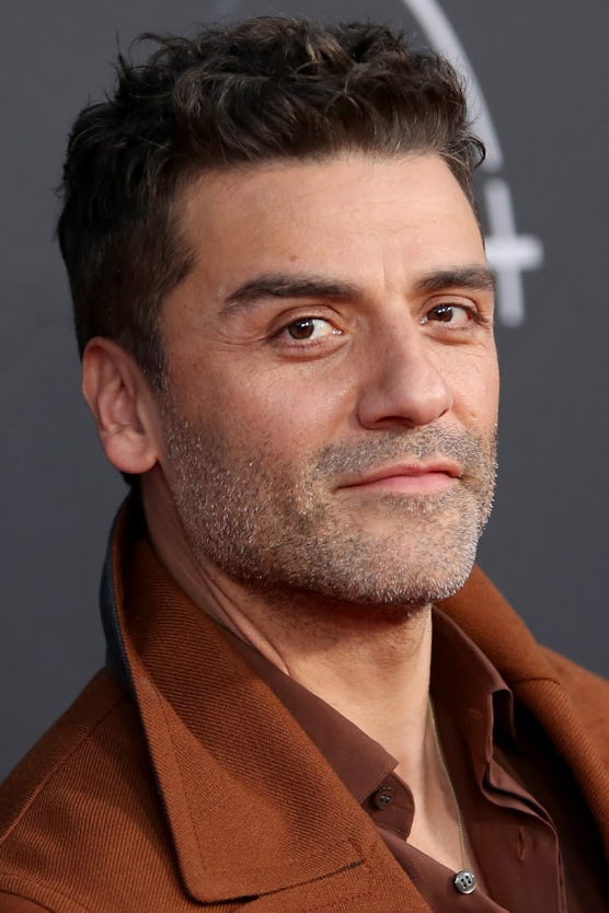 Oscar Isaac wearing a brown shirt and jacker with a five o clock shadow at a red carpet event