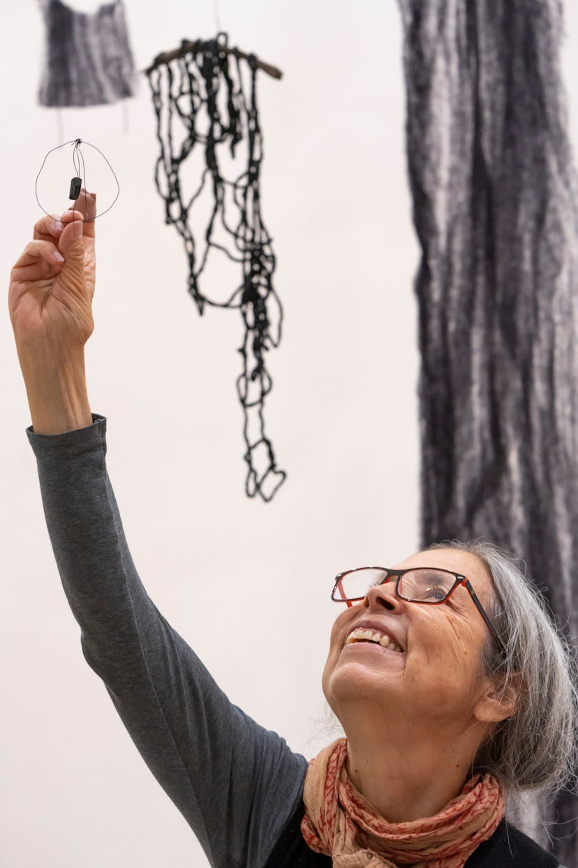 Cecilia Vicuña in her exhibition reaching toward a piece of art