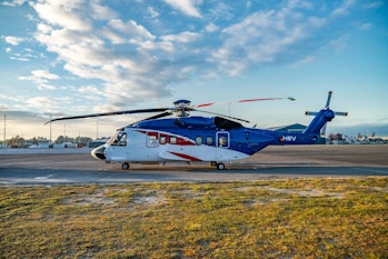 A helicopter painted blue and white sits on a runway that is flanked by grassy land. The sky is a li...