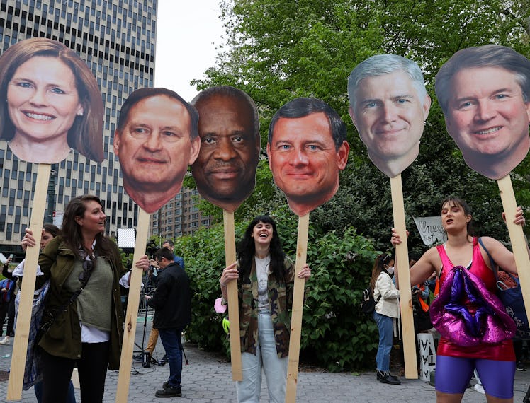 Protestors hold up posters of enlarged faces of Supreme Court justices 