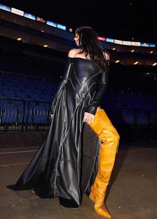 Dua Lipa wearing a long black dress with a slit and ultra-lengthy boots