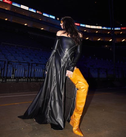 Dua Lipa wearing a long black dress with a slit and ultra-lengthy boots